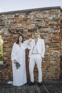 Portrait of confident newly married couple standing against brick wall