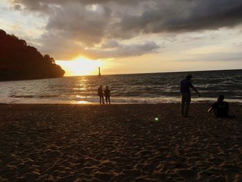 Silhouette people on beach against sky during sunset