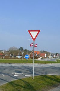Road sign by street against clear sky