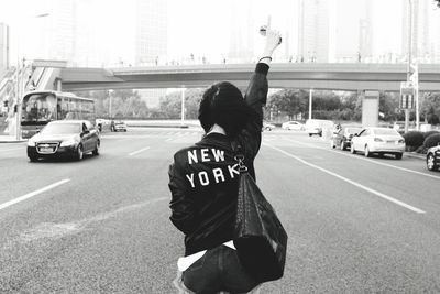 Rear view of woman with shoulder bag pointing while standing on street