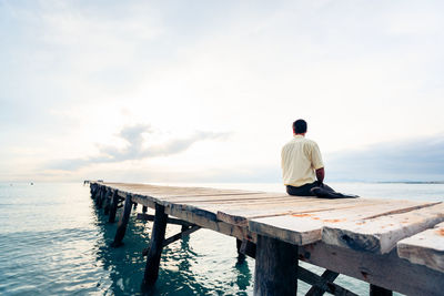 Businessman sitting on jetty over sea against sky