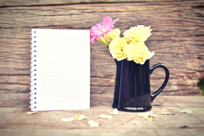 Yellow and pink flowers in pitcher with spiral notebook on wooden table