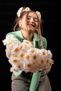 Smiling young woman holding flower against black background