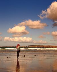 Full length rear view of woman walking at beach against cloudy sky
