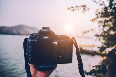 Reflection of person photographing on camera against sky during sunset