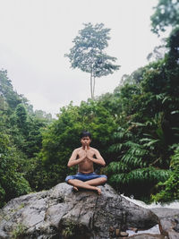 Young man sitting on rock against trees
