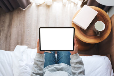 Midsection of woman using digital tablet while sitting on bed at home