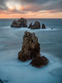 Rocks in sea against sky during sunset