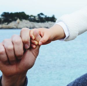 Close-up of couple holding hands against sea