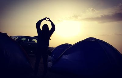 Silhouette of woman standing by tent on field against sky during sunset