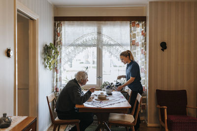 Senior man talking to female caregiver watering plants at home