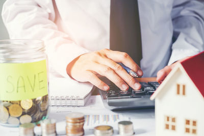 Midsection of businessman using calculator by jars with coin and model home
