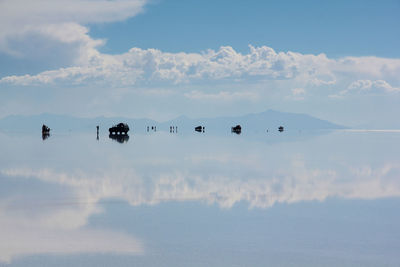 Tourists and vehicles reflection in water at salar de uyuni against sky