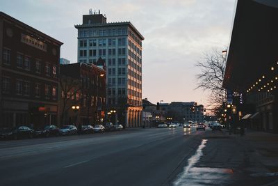 Cars on street amidst buildings in city at sunset