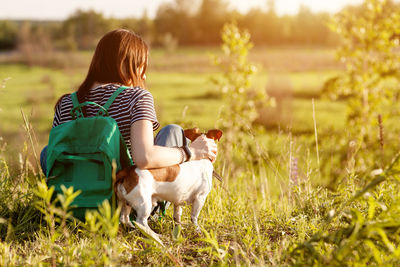 A dark-haired girl with a green backpack on her back and a striped t-shirt hugs a dog
