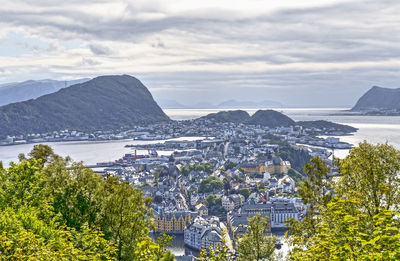 High angle view of cityscape by sea against cloudy sky