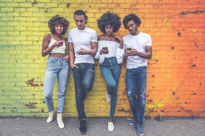 Full length portrait of friends standing against brick wall