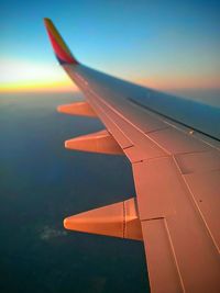 Close-up of airplane wing against sky during sunset