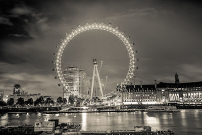 Illuminated millennium wheel by thames river in city at night