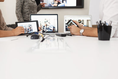 Midsection of business people with technologies at table in office