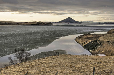 View during sunset over partly frozen lake myvatn in iceland, surrounded by grassy hills 