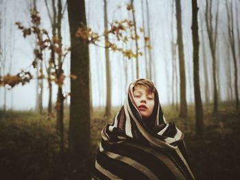 Boy with eyes closed wrapped in blanket at forest during winter