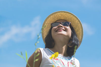 Low angle view of smiling woman in sunglasses and sun hat against sky