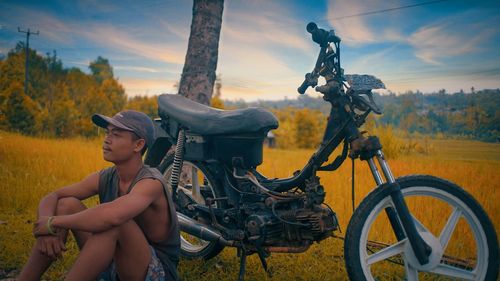 Young man sitting against old moped on field