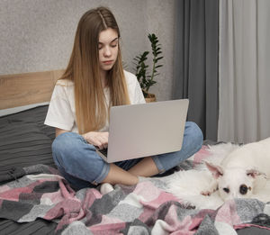 Girl using laptop by dog on bed at home