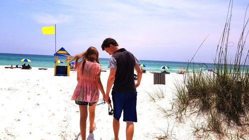 Rear view of siblings walking at beach against sky