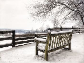 Empty benches on snow field against sky during winter