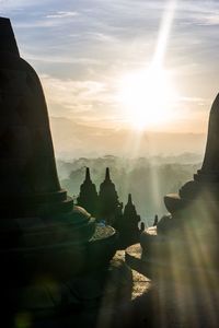 Silhouette temples against cloudy sky during sunny day