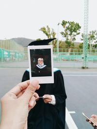 Cropped hand holding instant print transfer against person standing at court