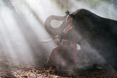 Smiling woman sitting with elephant in forest