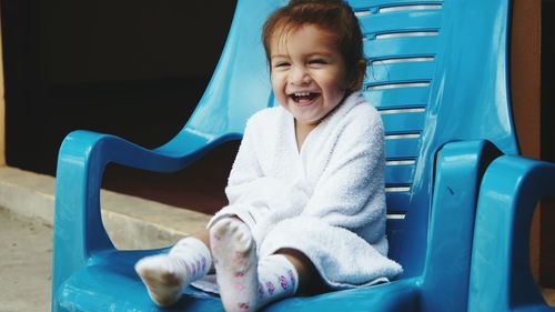 Cute smiling girl wrapped in towel sitting on blue chair