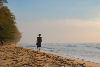 Silhouette man walk on beach with sunrise and sea background