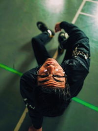 High angle portrait of young man wearing eyeglasses while sitting on sports court