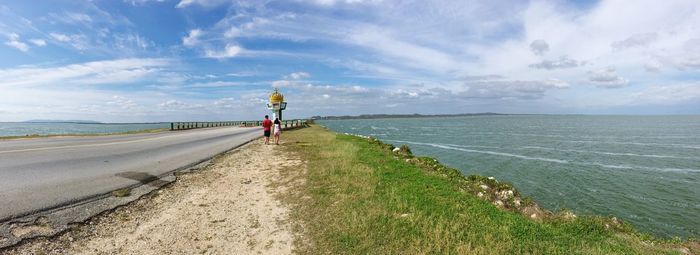 Man on road by sea against sky