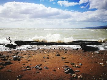 Sea waves splashing on shore against sky