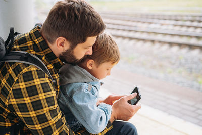 Back shot of caucasian man holding children hands walking along platform going to take train