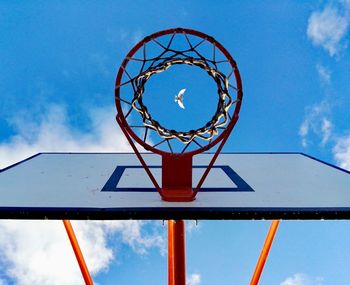 Low angle view of bird flying against sky seen through basketball hoop