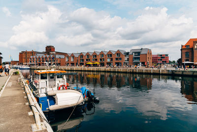 Boats moored on river by buildings in city against sky