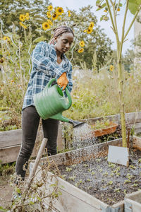 Young female volunteer watering plants in urban farm