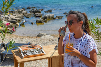 Young woman using telephone and having drink at beach