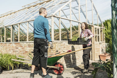 Woman carrying plant crate while talking to man at community garden