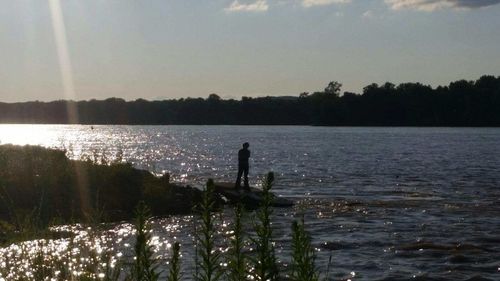 Silhouette of person standing by lake against sky