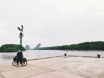 Man riding bicycle on street by lake against sky