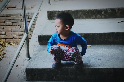 Cute boy looking up while sitting on staircase