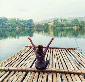 Woman gesturing peace sign while sitting on wooden raft in lake