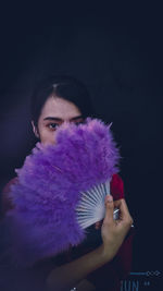 Portrait of woman holding purple flower against black background